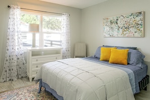 Een slaapkamer met een bed, een dressoir, een radiator en een raam met gordijnen.