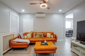 Una sala de estar moderna con sofá, reposapiés y ventilador de techo.