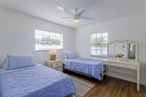 Un dormitorio con dos camas, un ventilador de techo, un aparador y una ventana con vista a la vegetación.