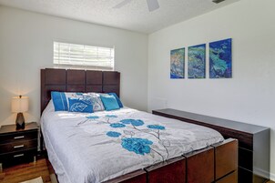 Un dormitorio con cama, mesitas de noche, persianas en una ventana y decoración en la pared.