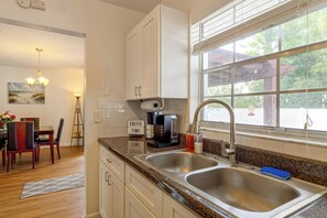 Una cocina con un lavamanos doble, una cafetera y un ventanal con vistas a árboles.
