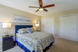 Une chambre à coucher comprenant un lit, des tables de chevet, un ventilateur de plafond, une lampe fixée au mur et une porte.