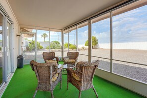 Un espace extérieur aménagé, abrité et doté de meubles en osier et d’une table en verre, offrant une vue sur un jardin paysager et un ciel dégagé.