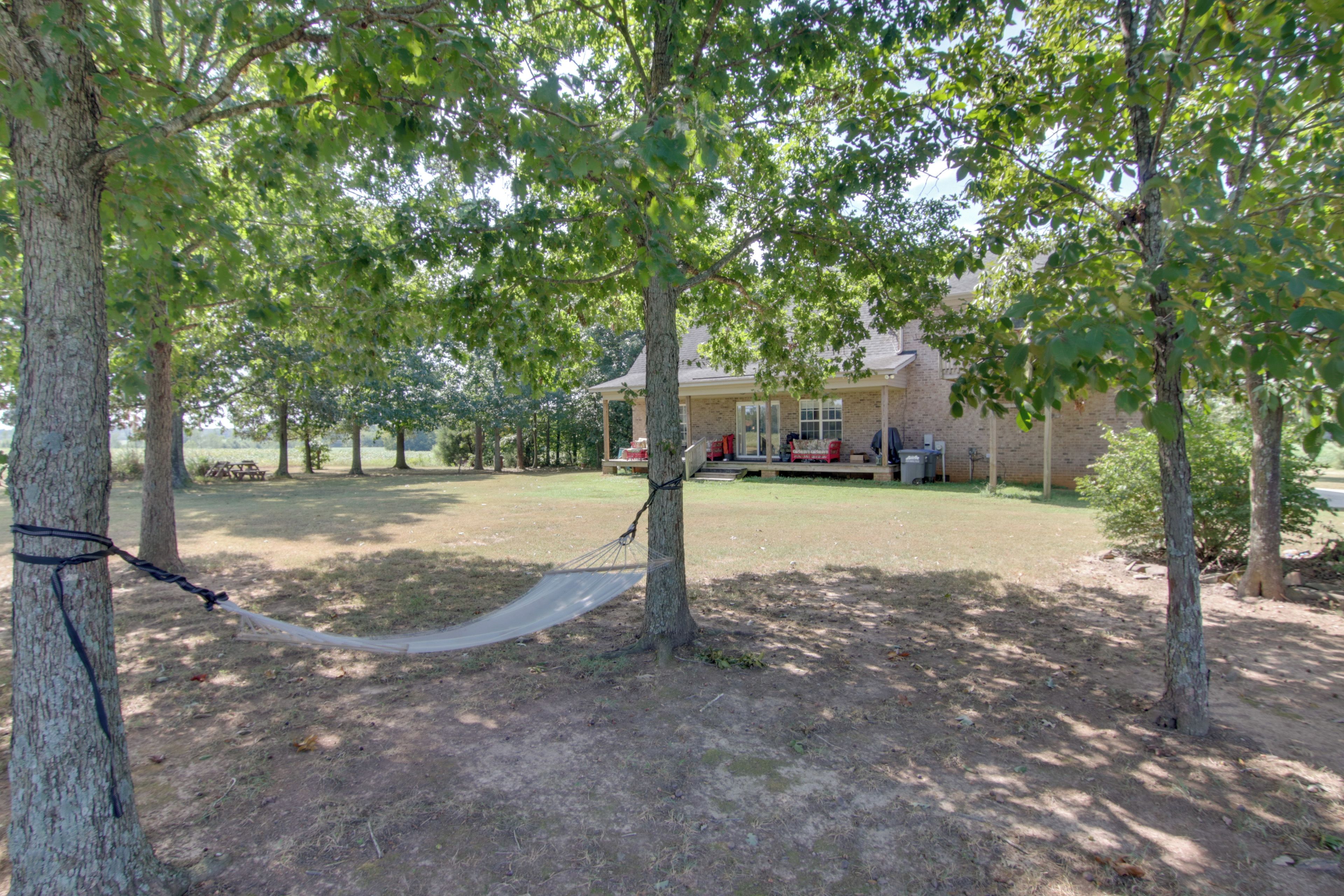 A backyard with a hammock, trees, and a house with a porch.