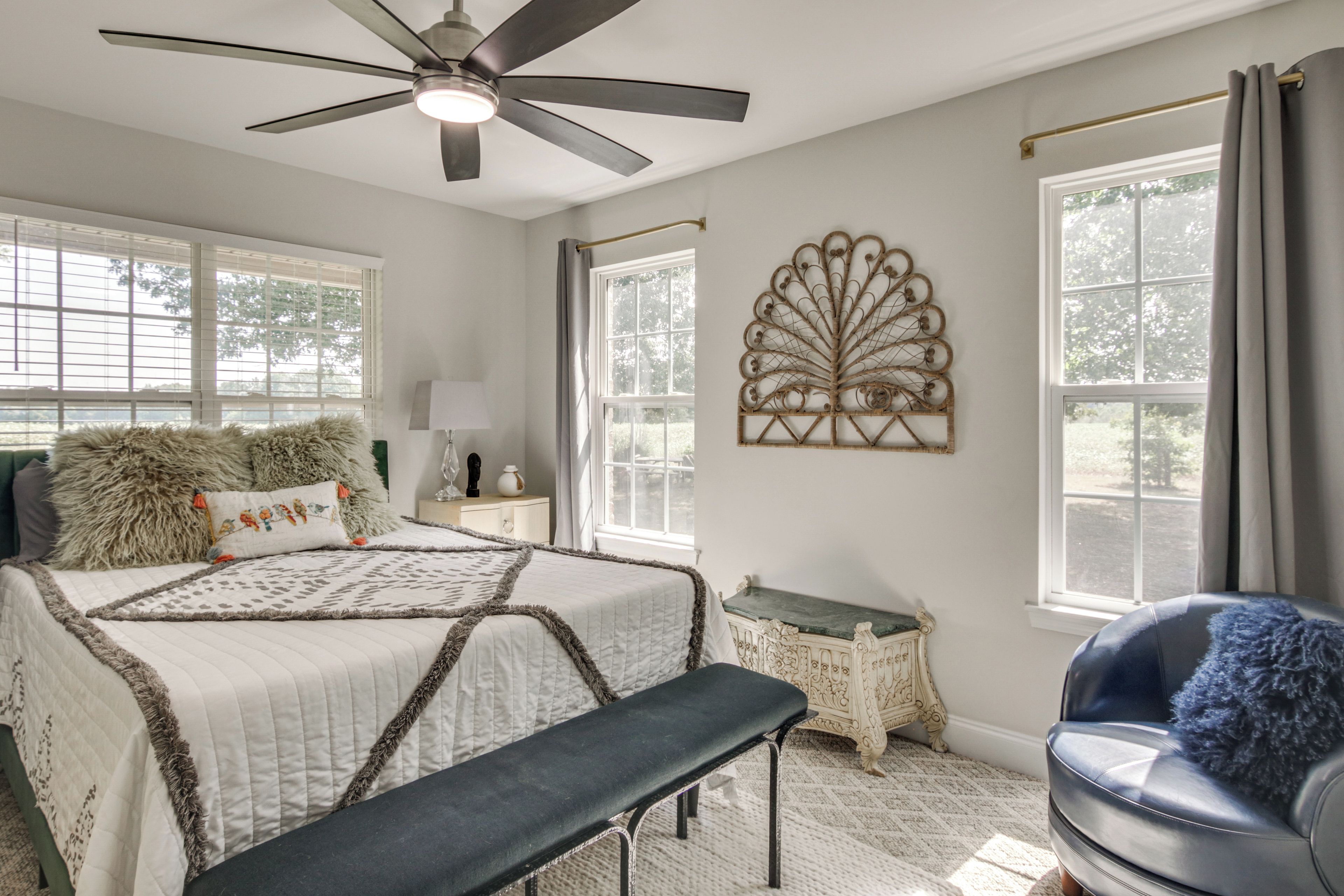 A bedroom with a bed, a bench, a chair, a ceiling fan, and a decorative wall piece.