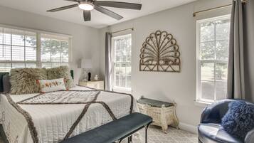 A bedroom with a bed, a bench, a chair, a ceiling fan, and a decorative wall piece.