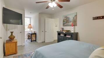 A bedroom with a bed, a ceiling fan, a desk with a lamp, a bookshelf, and a painting on the wall.