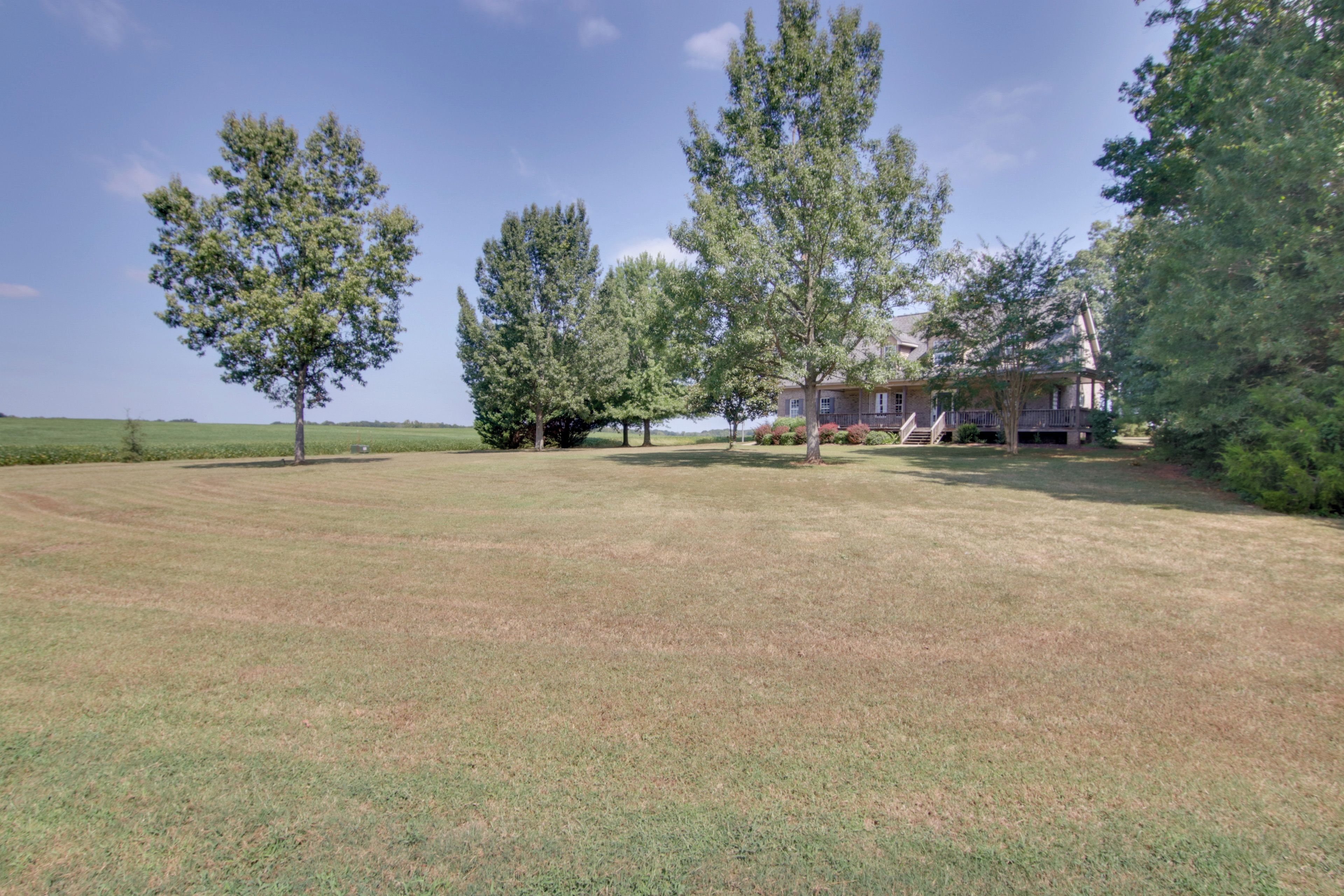 A property with a large lawn, several mature trees, and a two-story house with a porch.