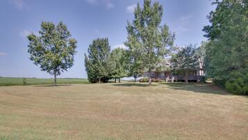 A property with a large lawn, several mature trees, and a two-story house with a porch.