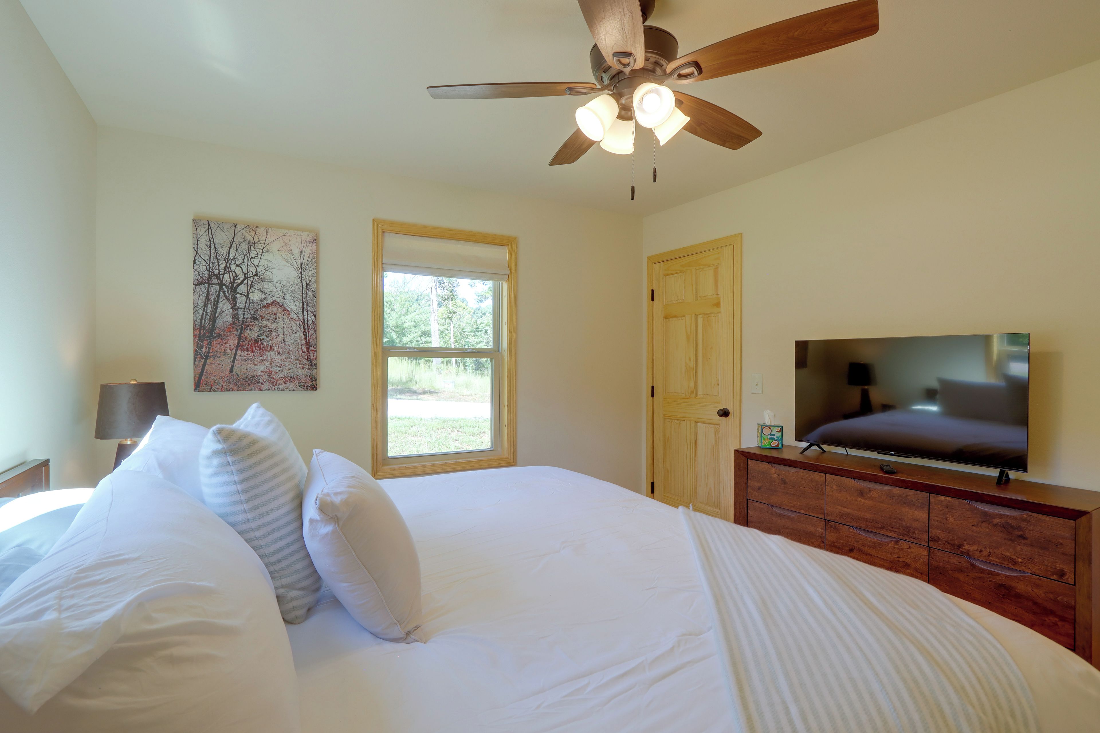A bedroom with a bed, a ceiling fan, a television, and a window.