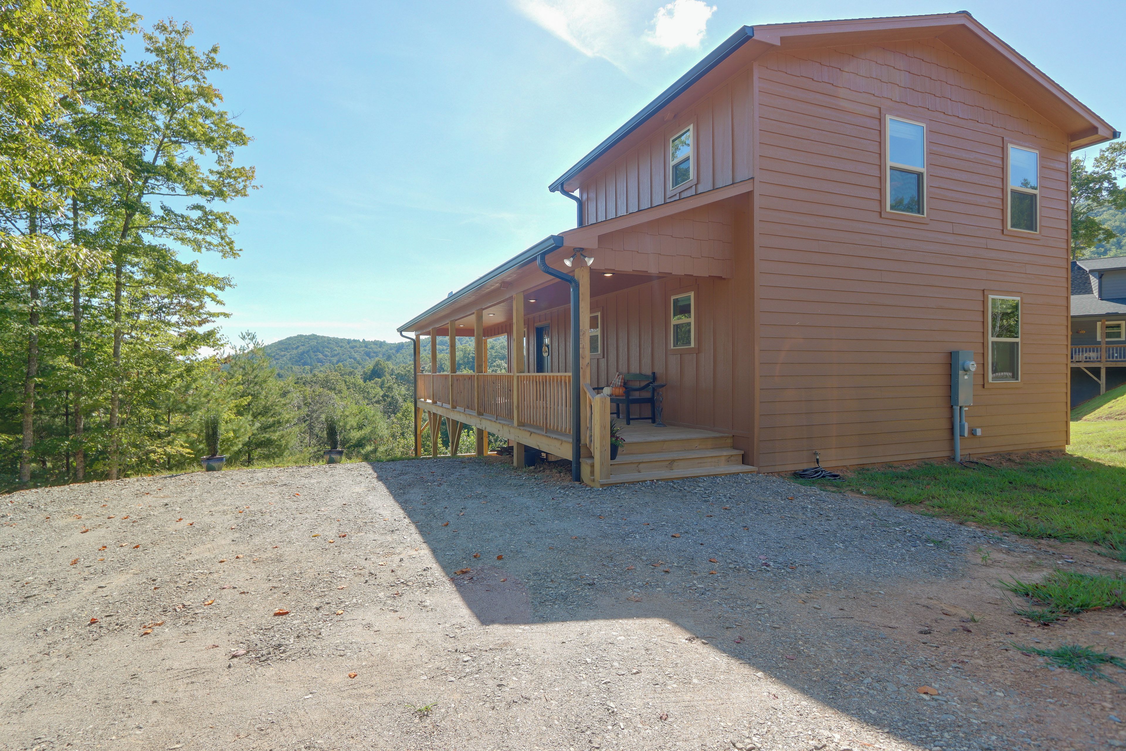 A two-story wooden cabin with a covered porch and a gravel driveway.