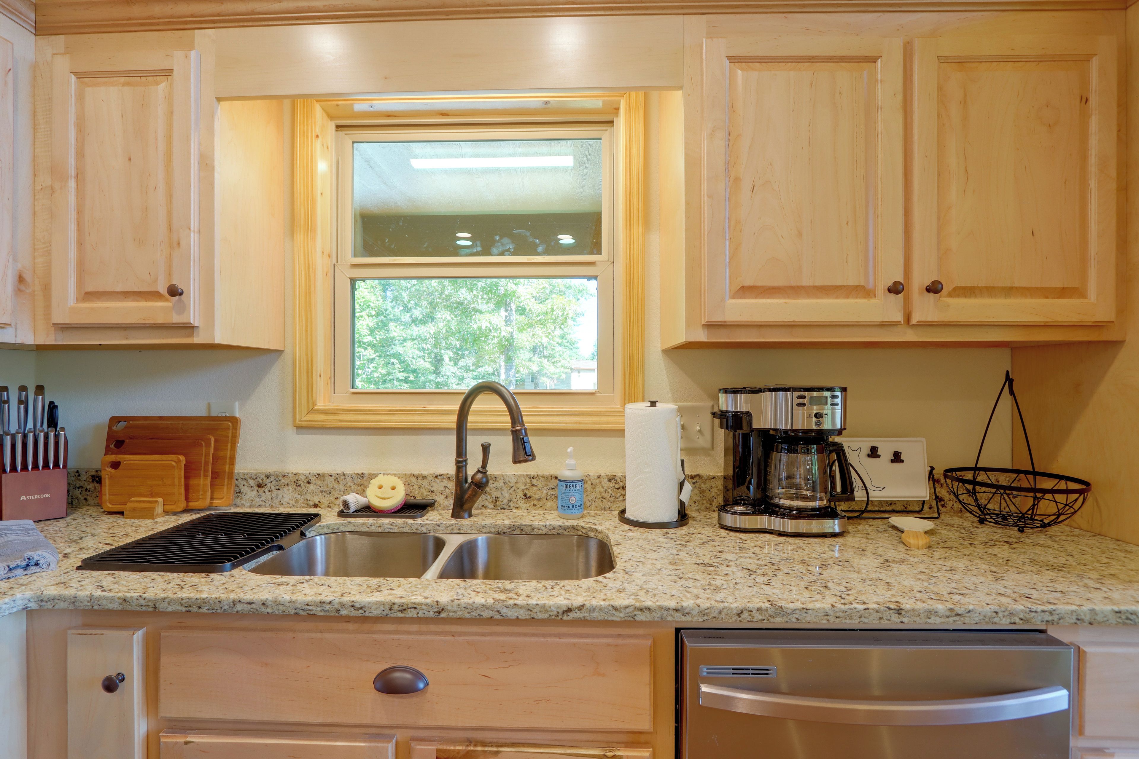 A kitchen with wooden cabinets, a stainless steel sink, a coffee maker, and a dish rack.