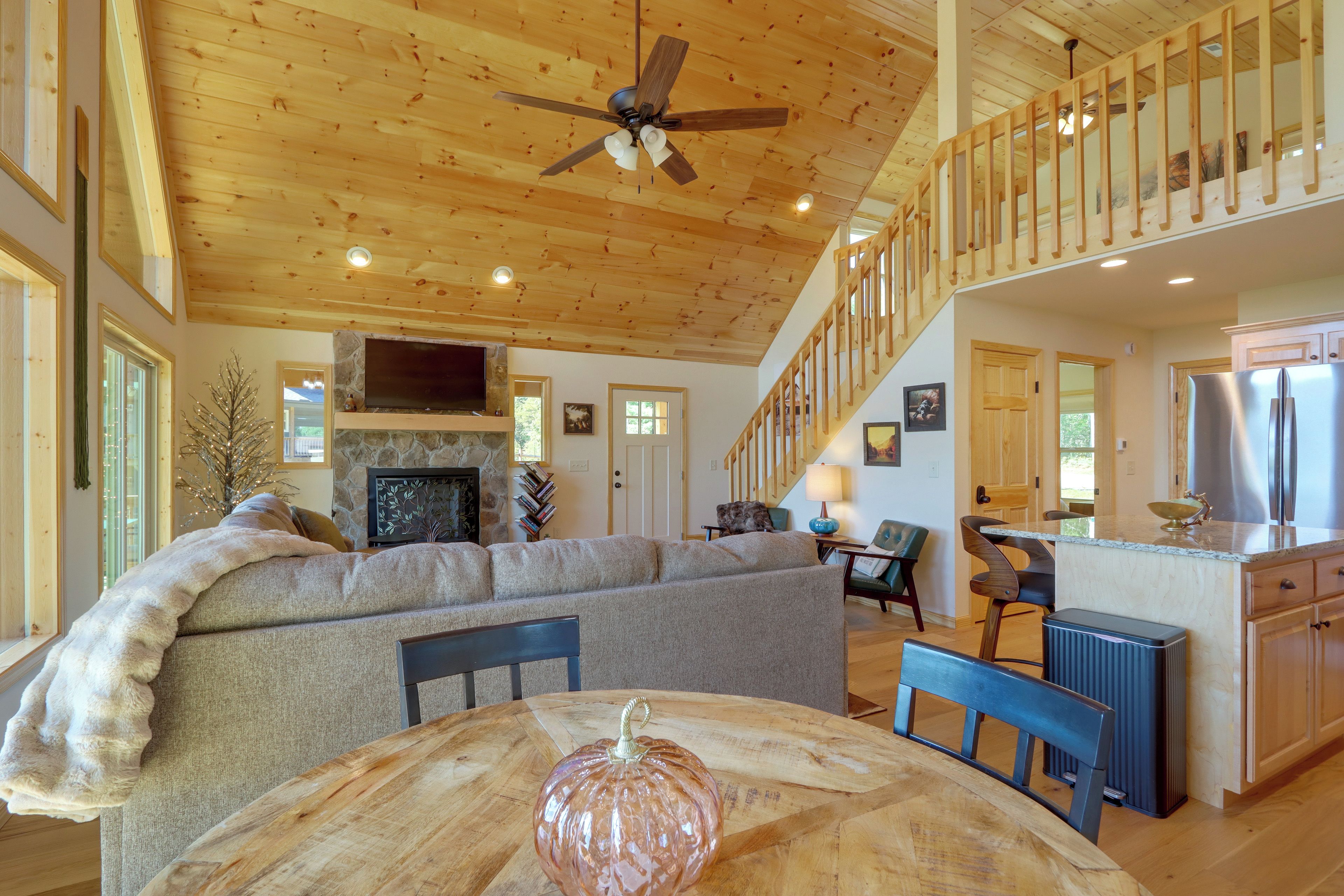 A spacious living area with a fireplace, a large sofa, a dining table with chairs, and a kitchen area with a refrigerator.