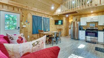 Interior acogedor de una cabaña con comedor, cocina y un sofá rojo con cojines estampados.