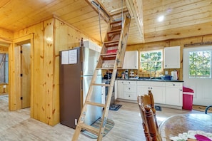L’intérieur d’une cabane en bois comprend une cuisine, un réfrigérateur, une échelle en bois et une porte qui donne sur une autre pièce.