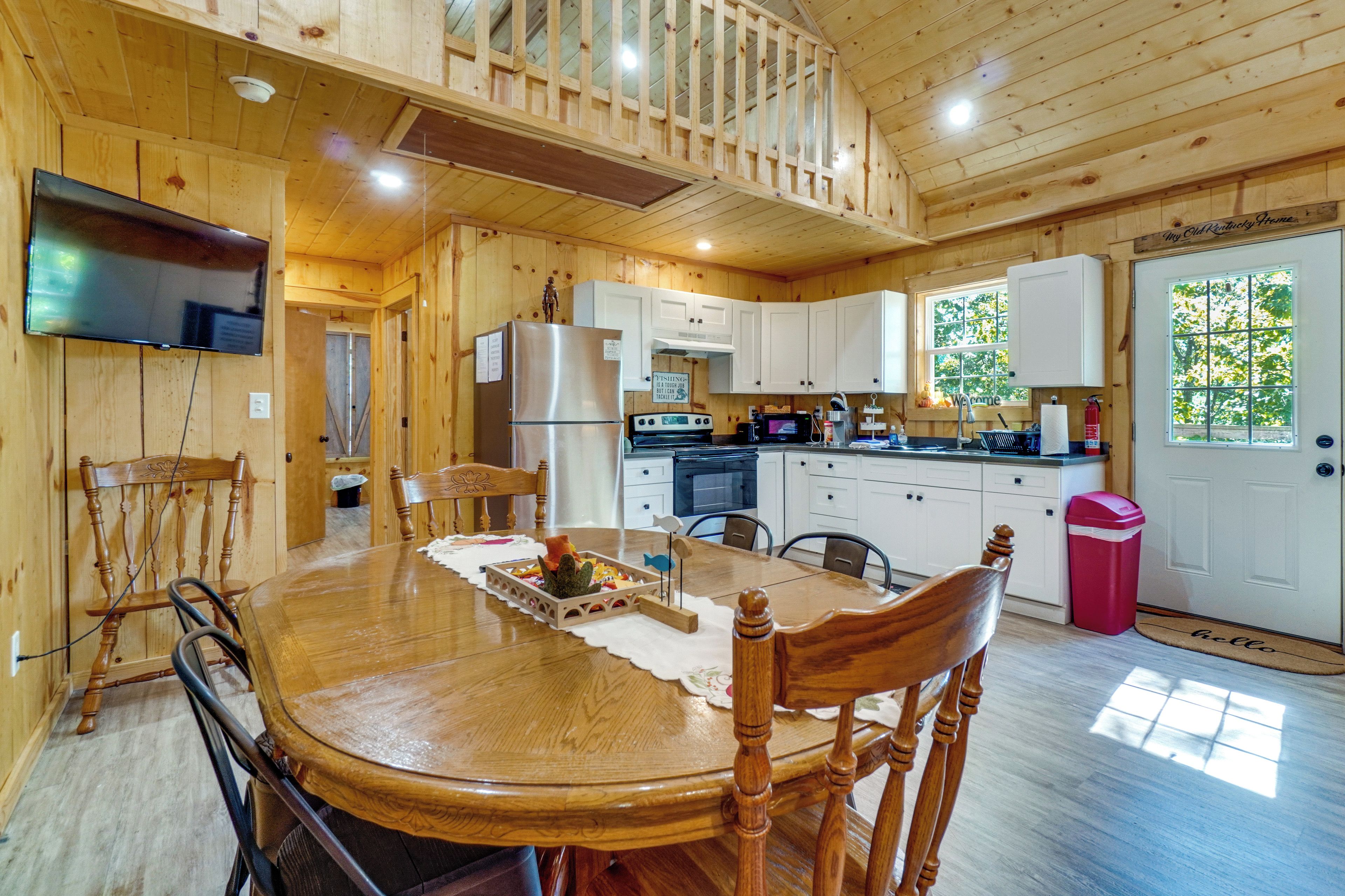 A wooden cabin interior with a dining table, chairs, a kitchen area, and a television mounted on the wall.
