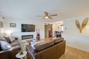 A modern living room with a fireplace, leather sofas, a flat-screen TV, and a dining area with a chandelier. - Walk to Lake & Downtown! 6 Mi to Boyne Mtn (Boyne City)