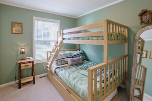 Una cama litera con una escalera, una mesita de noche con una lámpara, una ventana con persianas y un cuadro en la pared.