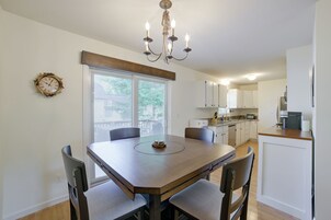 A dining area with a wooden table and chairs, a chandelier, and a wall clock.