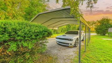 A covered car parking area with a gravel path leading to a white sports car.