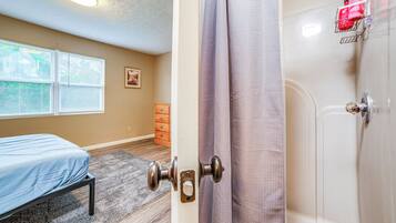 A bedroom with a bed, a dresser, and a shower.