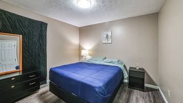A bedroom with a bed, a nightstand, a lamp, a framed picture on the wall, and a mirror with a dark curtain.
