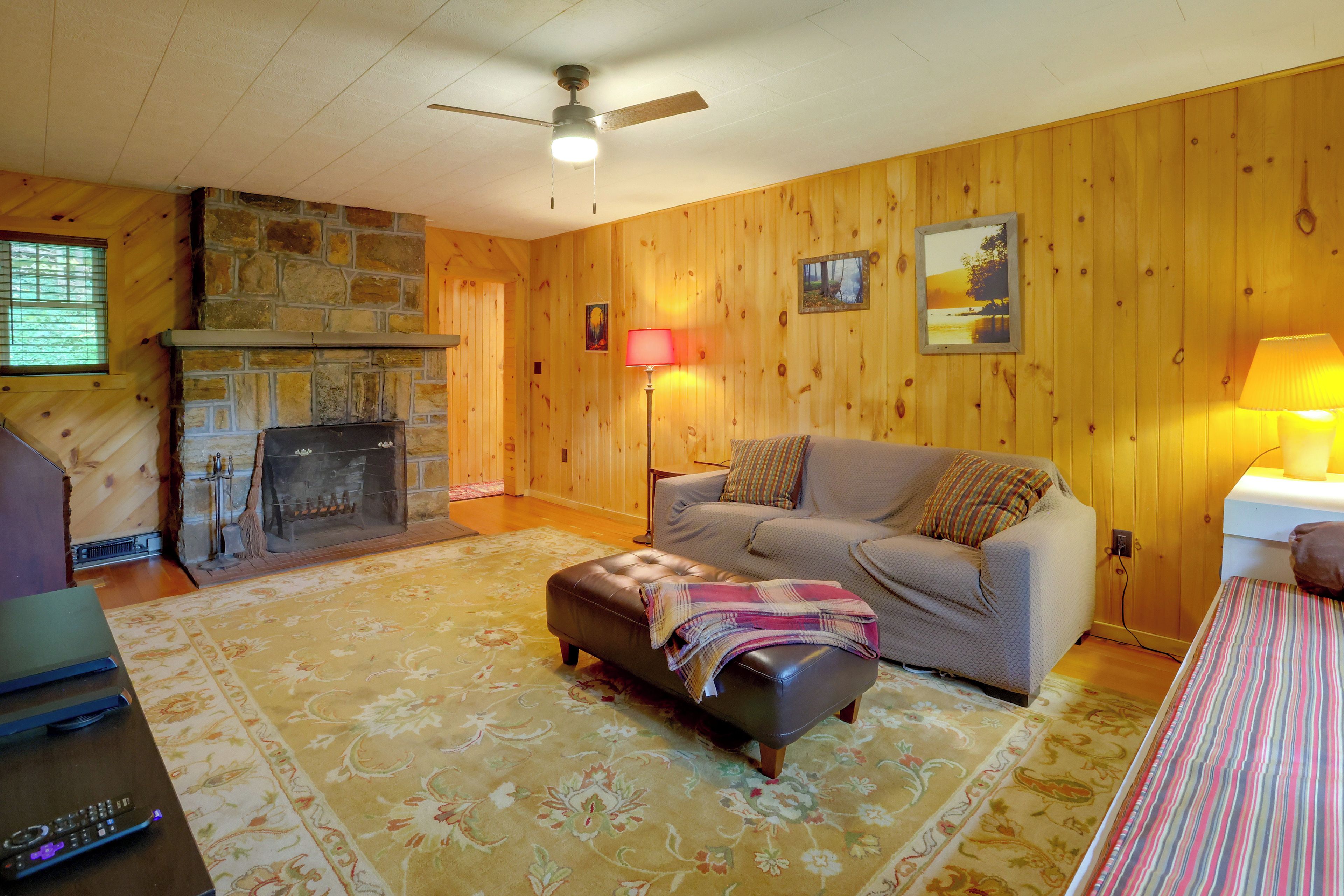Una sala de estar acogedora con chimenea, un sofá, una mesa de centro y un ventilador de techo.