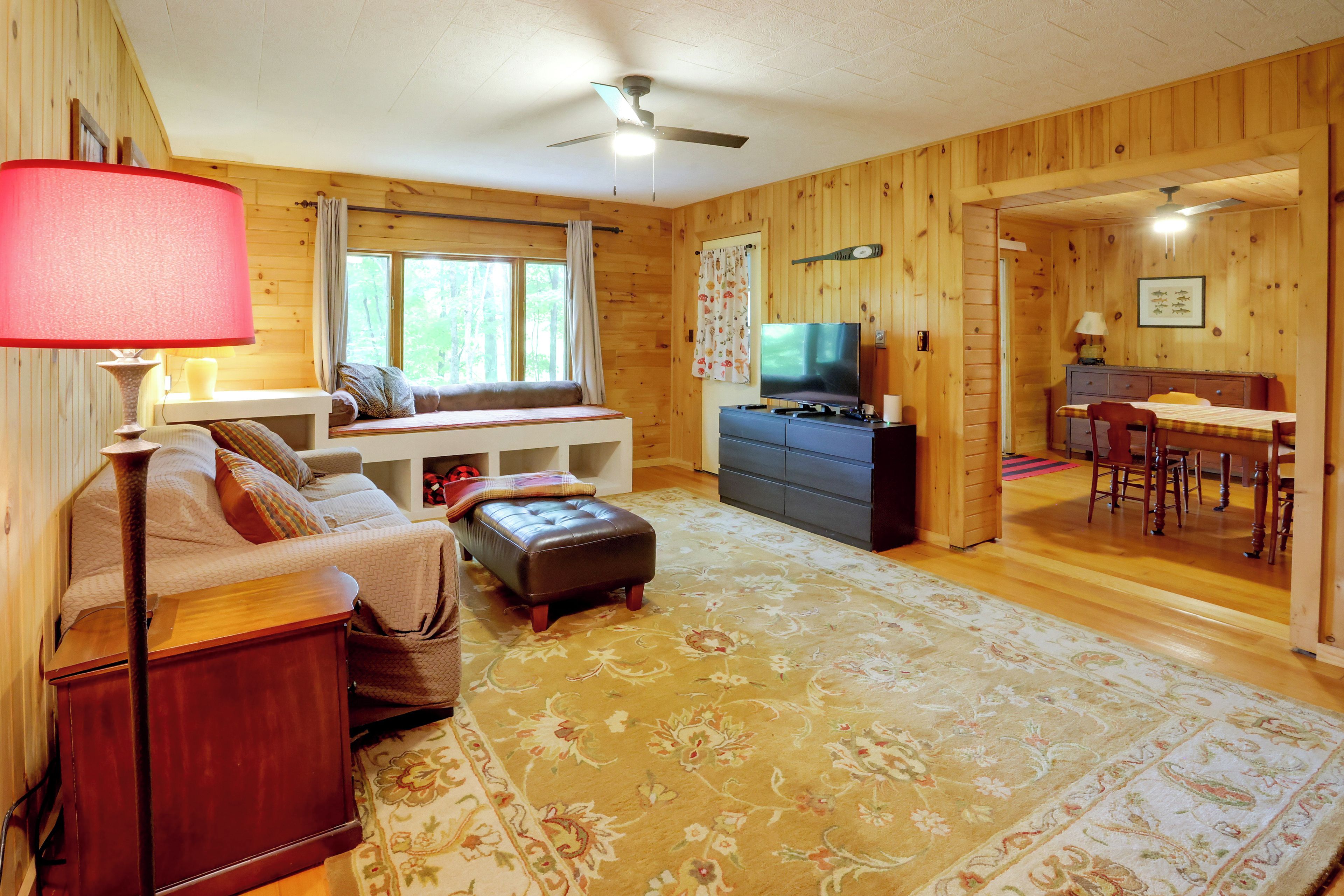 Un interior acogedor de cabaña con sofá, reposapiés, televisión y comedor.