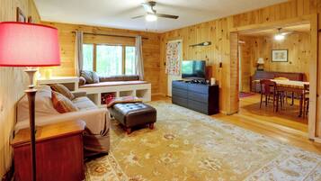 Un interior acogedor de cabaña con sofá, reposapiés, televisión y comedor.
