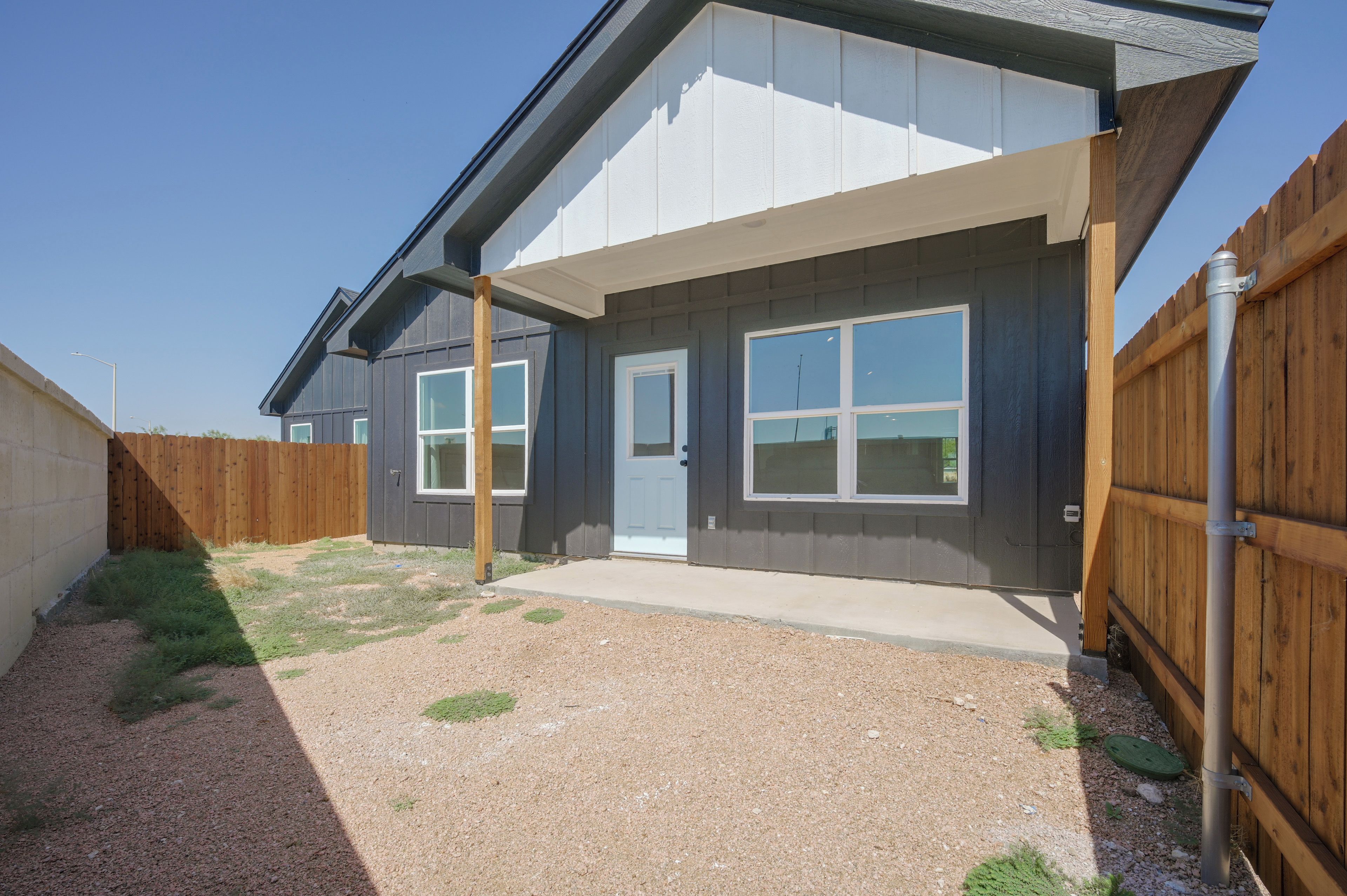 A residential building with a covered patio, a wooden fence, and a gravel driveway.