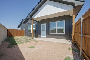 A residential building with a covered patio, a wooden fence, and a gravel driveway.