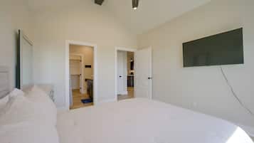 Quarto com cama, ventilador de teto e televisão fixada na parede.