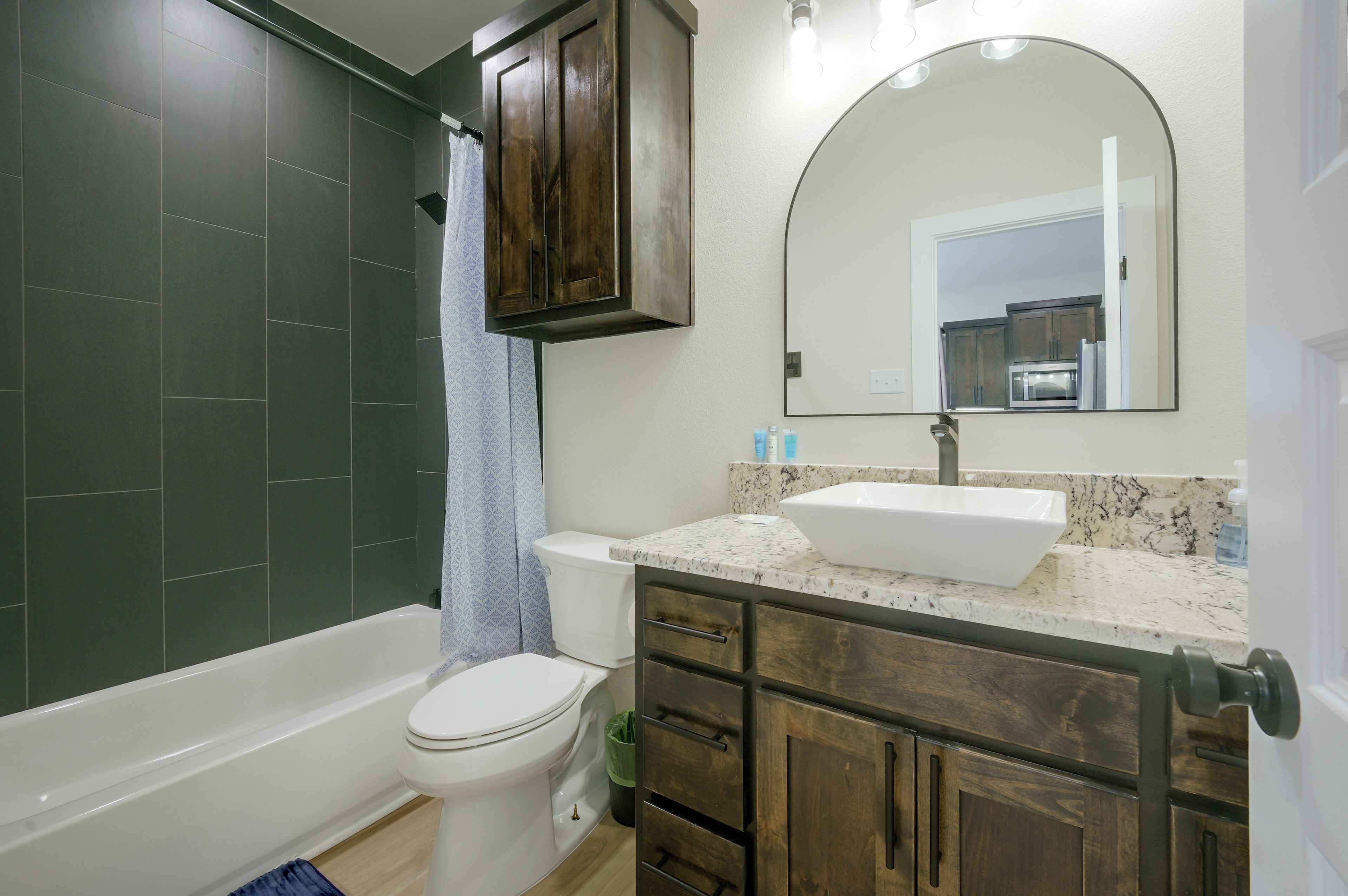 A bathroom with a bathtub, toilet, vanity with a sink, and a mirror.