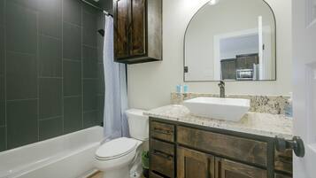 A bathroom with a bathtub, toilet, vanity with a sink, and a mirror.