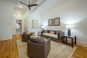 A spacious living room with a sofa, a coffee table, and a lamp. There is a door leading to a bathroom with a shower. - Main St Magic: Walkable Salisbury Condo! (Salisbury)