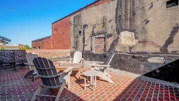A patio area with brick flooring, wooden furniture, and a brick wall with a window.