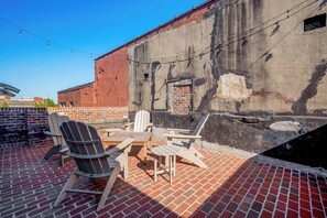 A patio area with brick flooring, wooden furniture, and a brick wall with a window. - Main St Magic: Walkable Salisbury Condo! (Salisbury)
