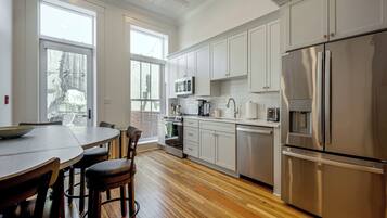 A modern kitchen with stainless steel appliances, white cabinetry, and a wooden floor.