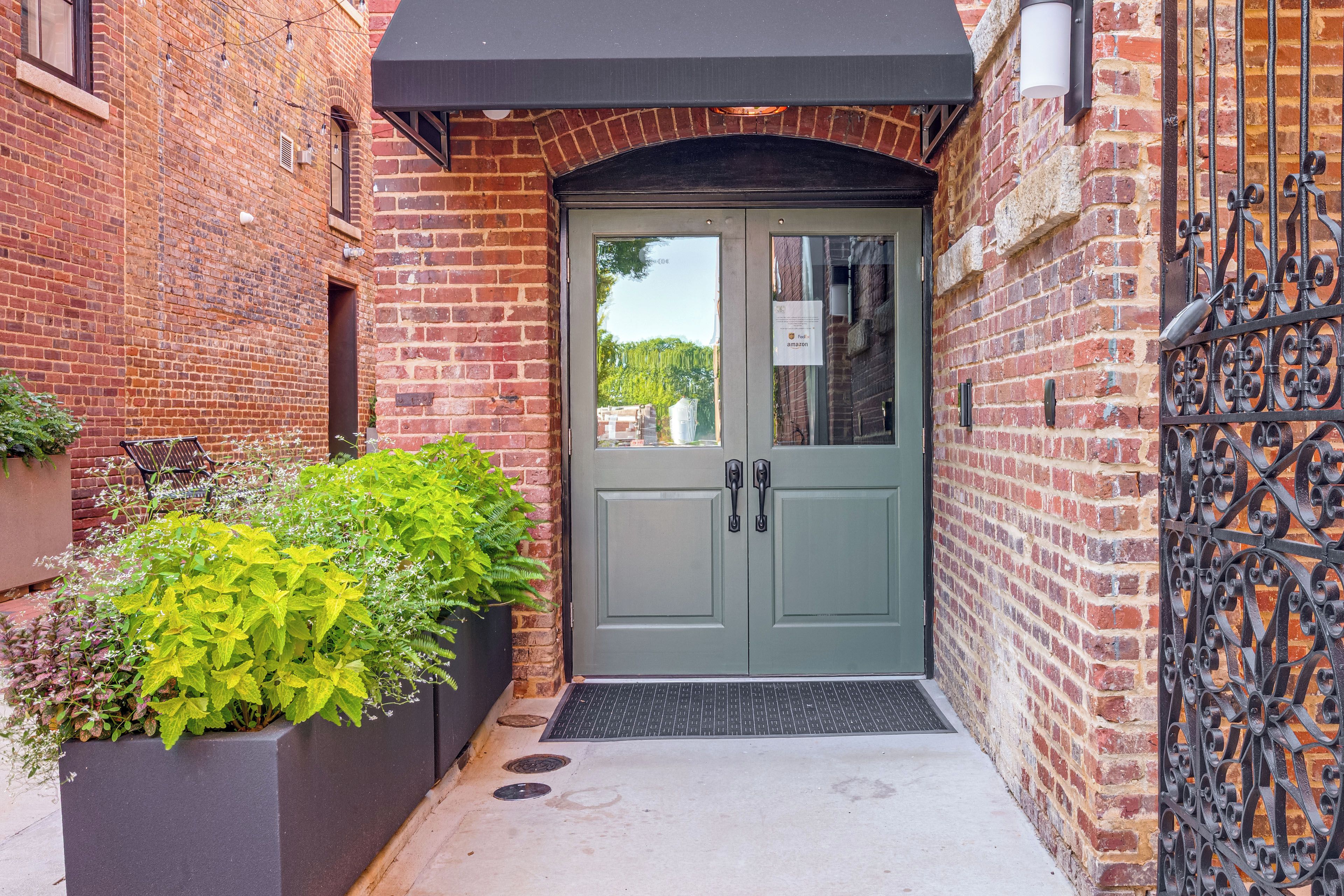 A brick building with a green double door, a black awning, and a metal gate.