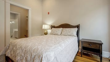 A bedroom with a bed, a nightstand, a lamp, and a door leading to a bathroom.