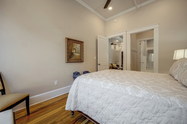 A bedroom with a large bed, a chair, a painting, and a bathroom visible through an open door. - Main St Magic: Walkable Salisbury Condo! (Salisbury)