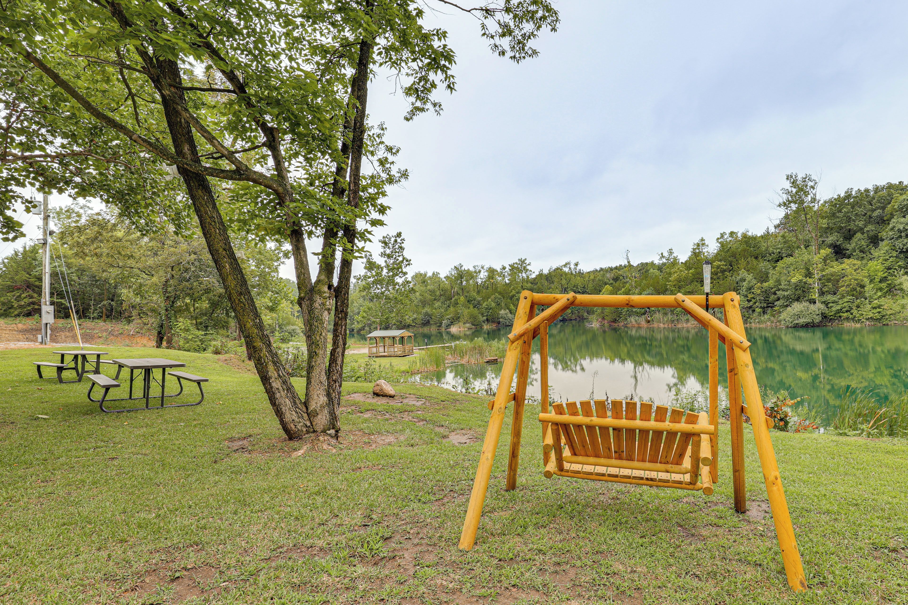 A park with a swing set, picnic tables, and a small gazebo by a lake.