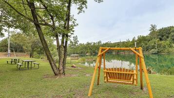 A park with a swing set, picnic tables, and a small gazebo by a lake.