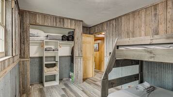 Habitación con literas de madera, un estante blanco y una puerta que da a otra habitación.