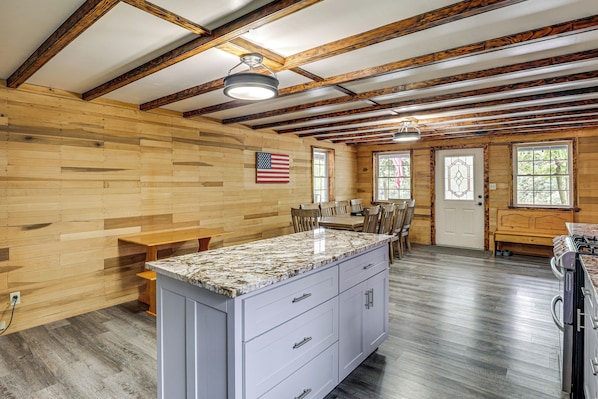 A spacious kitchen with a granite countertop, wooden beams, and a large window.
