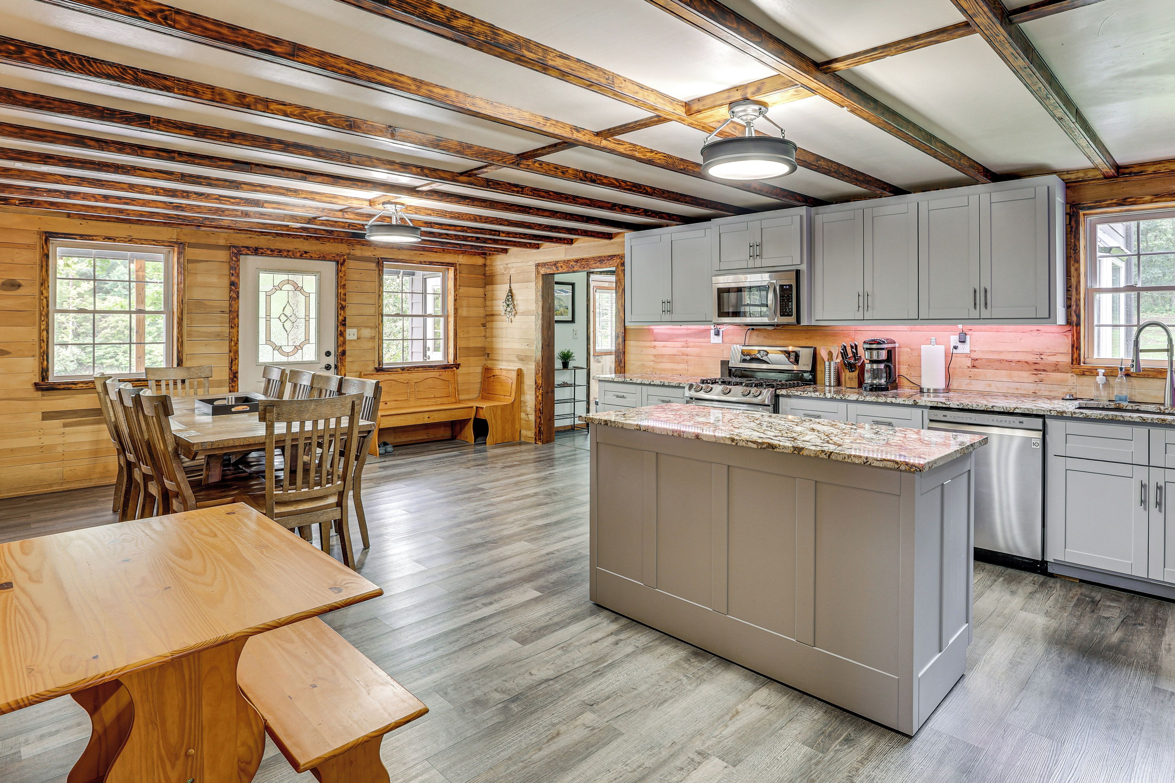 A spacious kitchen with a central island, wooden dining area, and large windows.