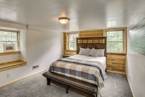 A bedroom with a wooden headboard, a bench, a bed with a quilt, and a window with a view of trees.