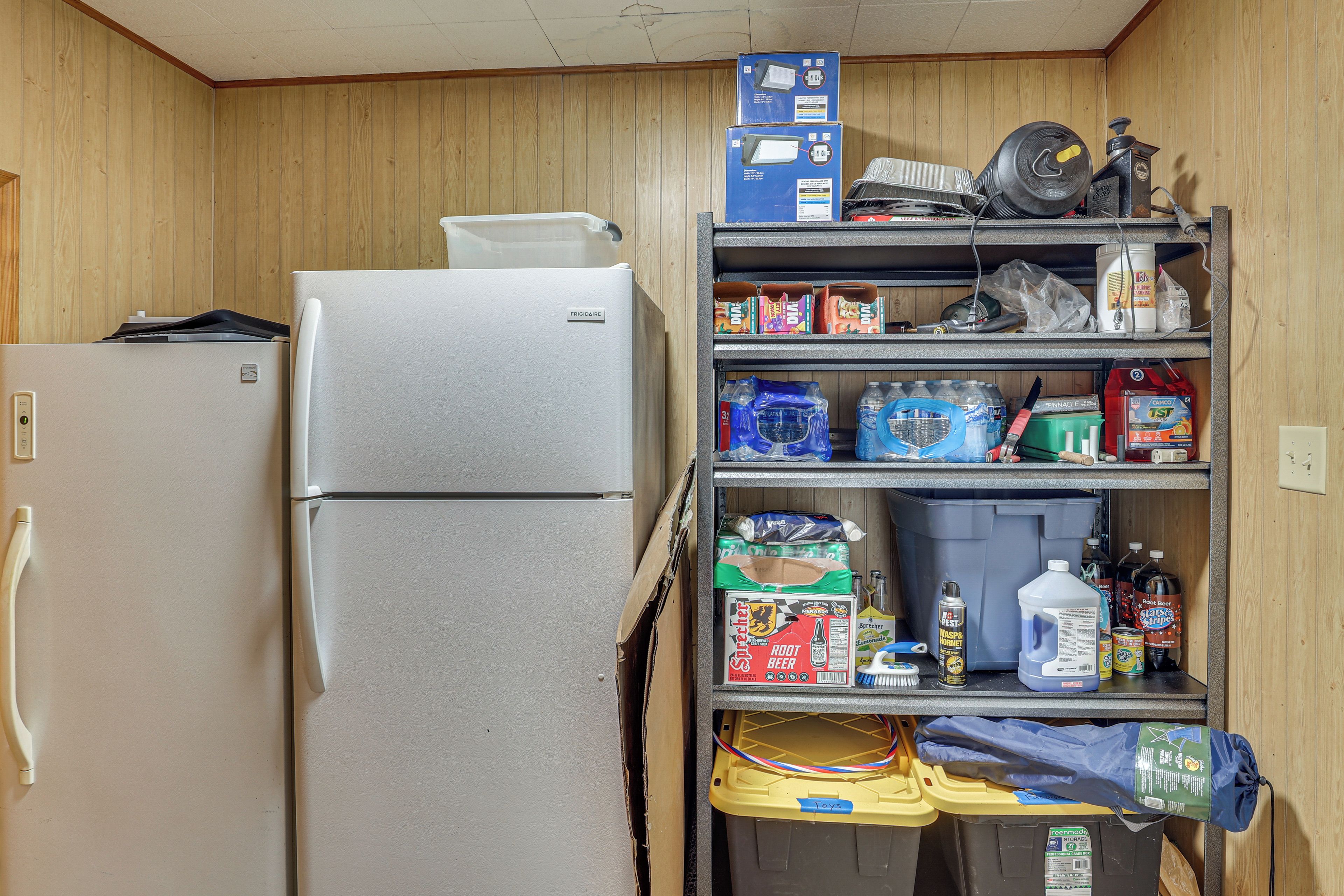A compact kitchenette with a refrigerator, shelves stocked with various food items, and a small storage area.
