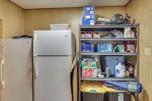 A compact kitchenette with a refrigerator, shelves stocked with various food items, and a small storage area.
