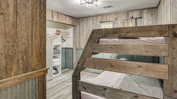 A bunk bed with a wooden frame, a white ceiling with a light fixture, and a white wardrobe with hanging clothes.